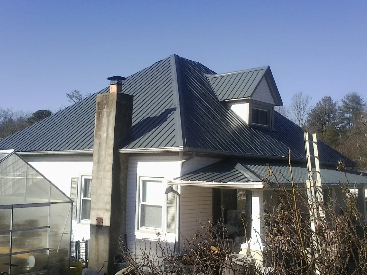 Dark blue standing seam metal roof on a white farmhouse with dormer — Slate & Tile Roof Repair by Roofing Brothers in West Union